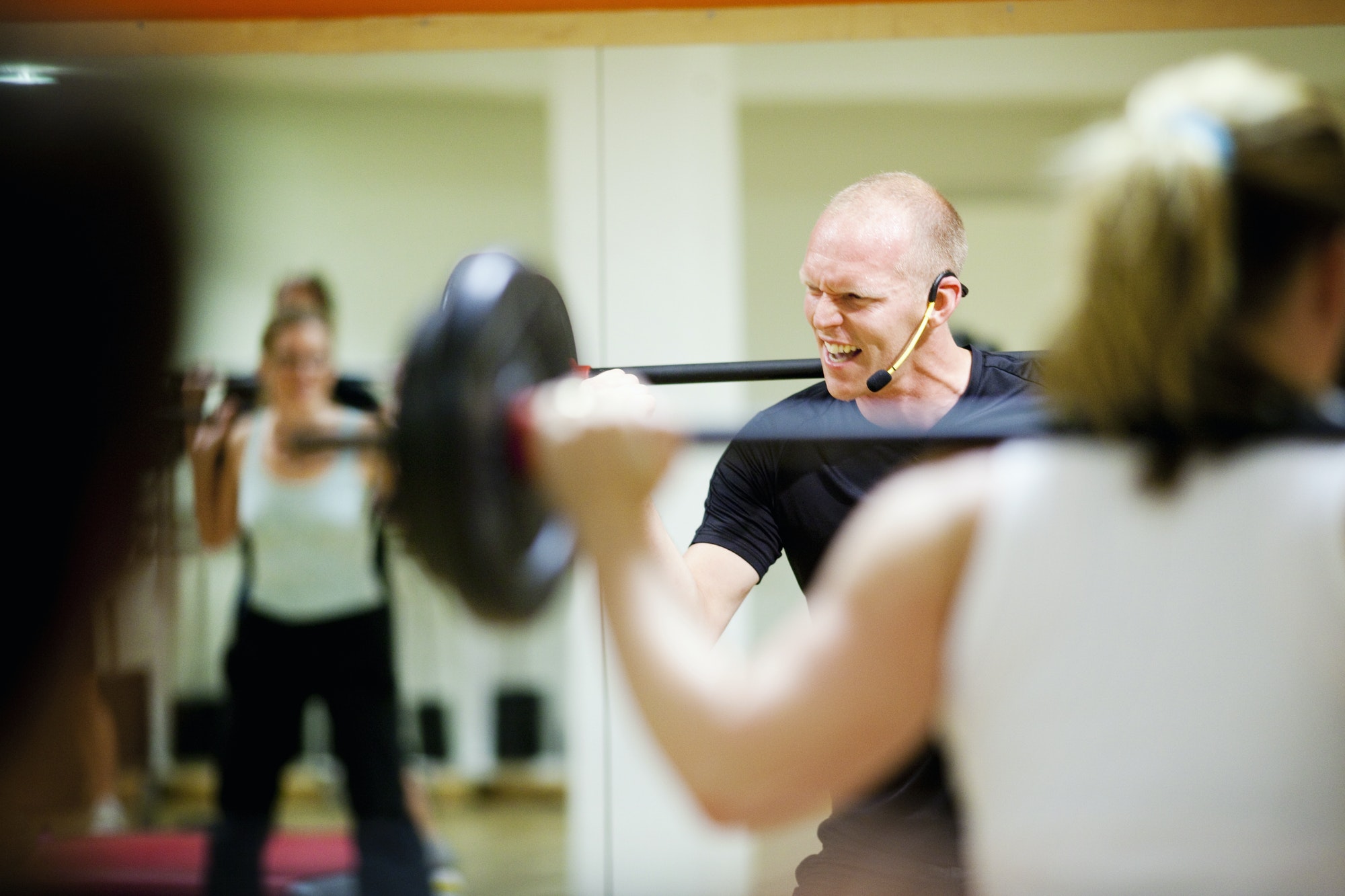 Cheerful instructor lifting barbell in class at gym