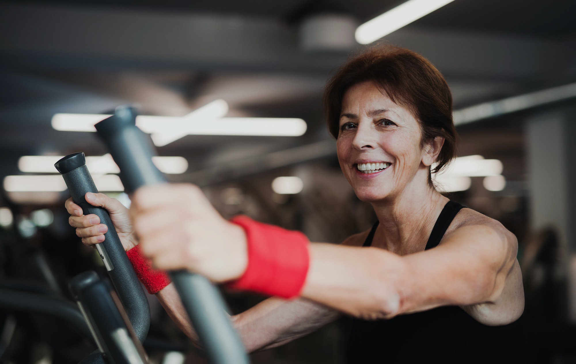 A cheerful female senior in gym doing cardio workout.